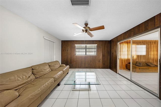 tiled living room with wooden walls, ceiling fan, and a textured ceiling