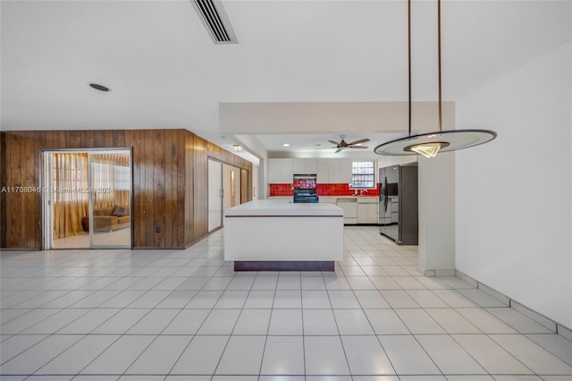 kitchen featuring ceiling fan, tasteful backsplash, wood walls, black range, and white cabinets