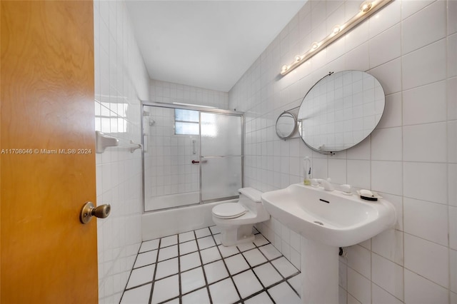 bathroom with combined bath / shower with glass door, backsplash, tile patterned floors, tile walls, and toilet