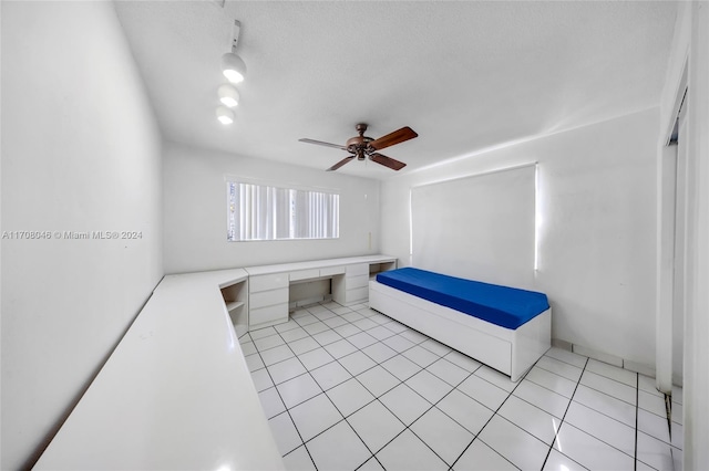 unfurnished bedroom featuring ceiling fan, light tile patterned floors, built in desk, and a textured ceiling