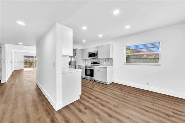 kitchen featuring white cabinets, light wood-type flooring, backsplash, and appliances with stainless steel finishes