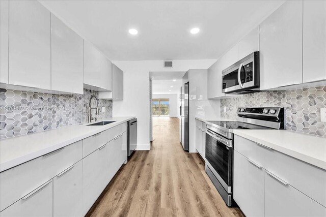 kitchen featuring white cabinets, sink, stainless steel appliances, and light hardwood / wood-style flooring