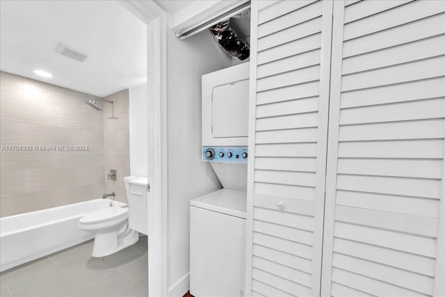 bathroom featuring tile patterned floors, stacked washer / dryer, tiled shower / bath combo, and toilet