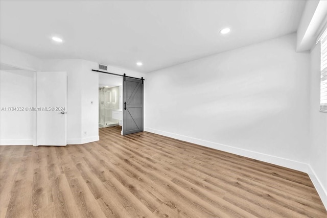 unfurnished bedroom featuring a barn door and light hardwood / wood-style floors