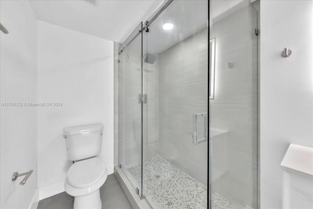 bathroom with tile patterned floors, toilet, and a shower with door