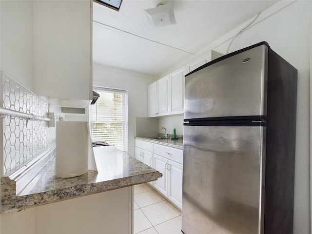 kitchen featuring backsplash, white cabinets, sink, light tile patterned floors, and stainless steel refrigerator