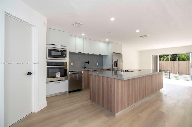 kitchen featuring sink, white cabinets, stainless steel appliances, a center island with sink, and light wood-type flooring