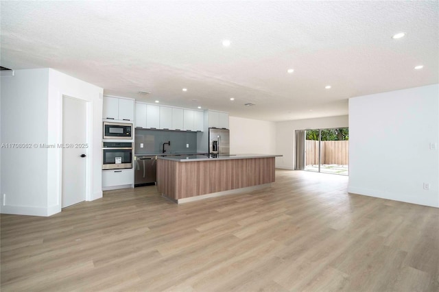 kitchen with an island with sink, appliances with stainless steel finishes, white cabinets, and light wood-type flooring