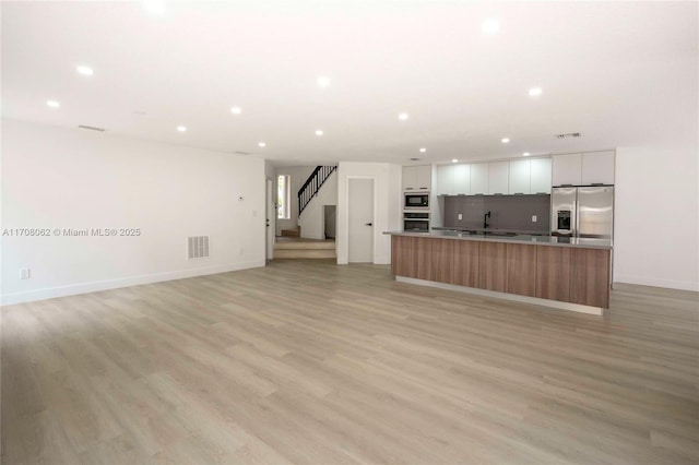 kitchen with a large island, white cabinets, built in microwave, stainless steel fridge with ice dispenser, and light wood-type flooring