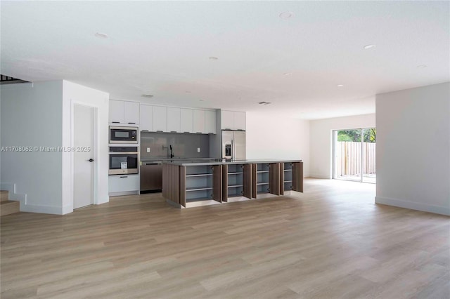 kitchen featuring appliances with stainless steel finishes, a center island with sink, white cabinets, and light hardwood / wood-style flooring