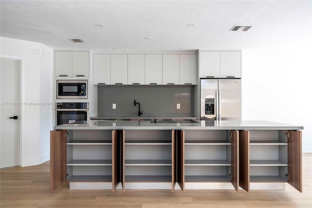 kitchen featuring stainless steel appliances, white cabinetry, a textured ceiling, and light hardwood / wood-style flooring