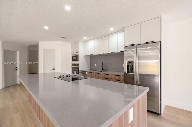 kitchen featuring white cabinetry, a textured ceiling, light wood-type flooring, appliances with stainless steel finishes, and a large island