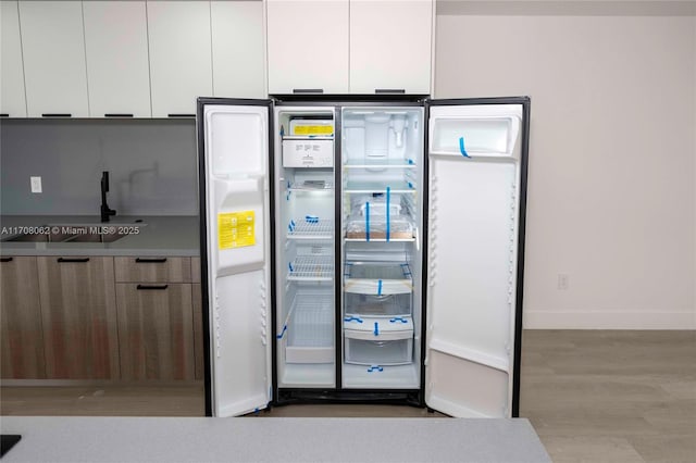 details with white cabinetry, light wood-type flooring, sink, and stainless steel refrigerator