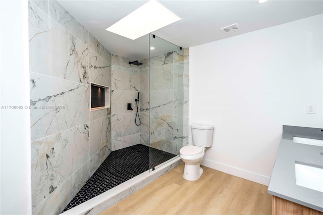 bathroom featuring a skylight, tiled shower, vanity, wood-type flooring, and toilet