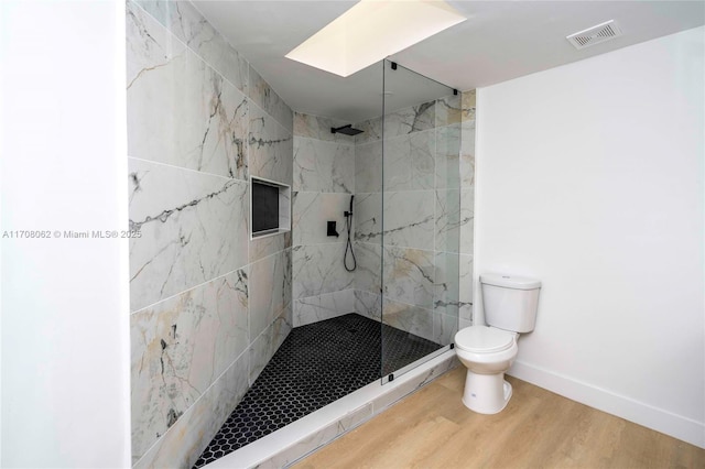 bathroom featuring tiled shower, wood-type flooring, toilet, and a skylight