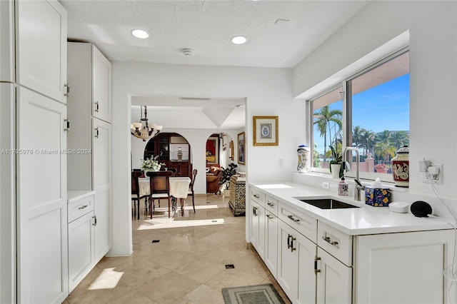 kitchen featuring white cabinets, a textured ceiling, an inviting chandelier, and sink