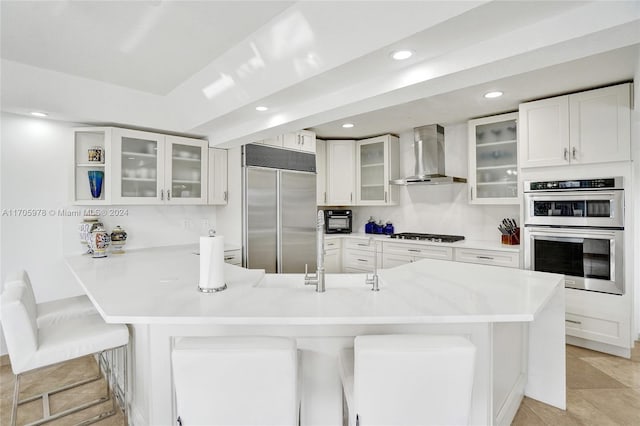 kitchen with appliances with stainless steel finishes, a breakfast bar, wall chimney range hood, white cabinets, and light tile patterned flooring