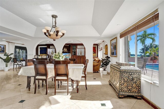 tiled dining space with a raised ceiling and a chandelier