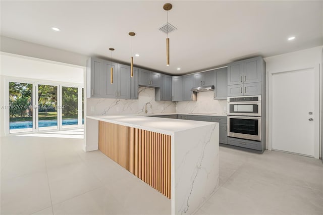 kitchen with backsplash, kitchen peninsula, hanging light fixtures, light stone countertops, and stainless steel double oven