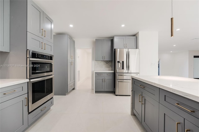 kitchen featuring appliances with stainless steel finishes, backsplash, light stone counters, gray cabinetry, and light tile patterned flooring