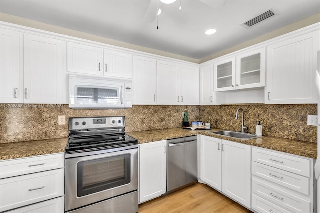 kitchen featuring sink, backsplash, appliances with stainless steel finishes, white cabinets, and light wood-type flooring