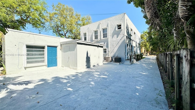 rear view of house with an outbuilding, central AC, fence, and stucco siding