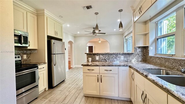 kitchen featuring stainless steel appliances, ceiling fan, light stone counters, sink, and decorative light fixtures