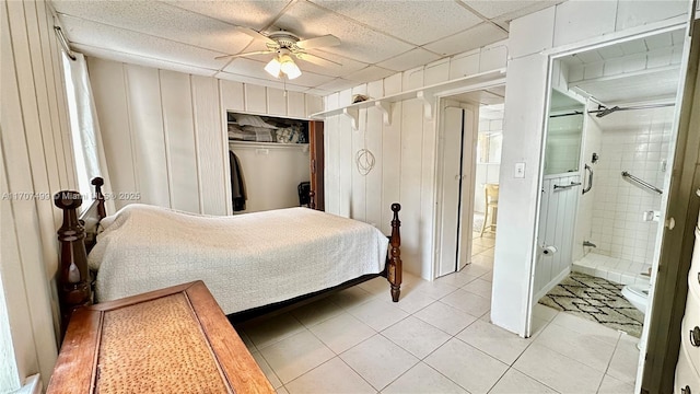 bedroom with a drop ceiling, ceiling fan, light tile patterned floors, a closet, and wood walls