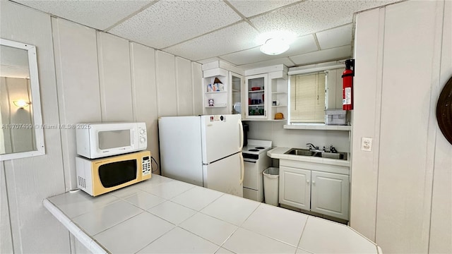 kitchen with white appliances, tile countertops, a paneled ceiling, white cabinetry, and sink