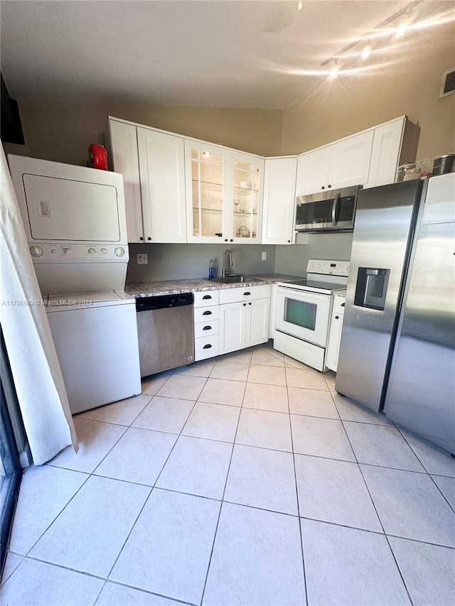 kitchen featuring lofted ceiling, sink, white cabinetry, stacked washer / dryer, and stainless steel appliances