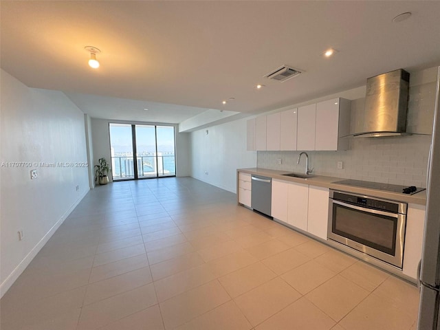 kitchen with tasteful backsplash, floor to ceiling windows, wall chimney exhaust hood, stainless steel appliances, and white cabinets