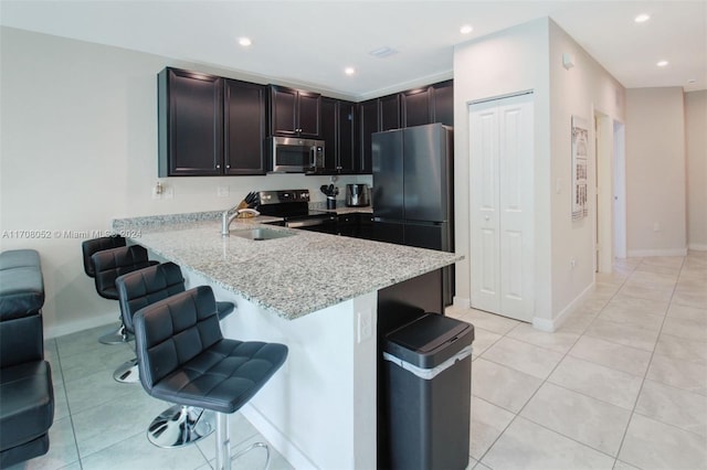 kitchen with light stone countertops, stainless steel appliances, kitchen peninsula, a breakfast bar area, and light tile patterned floors