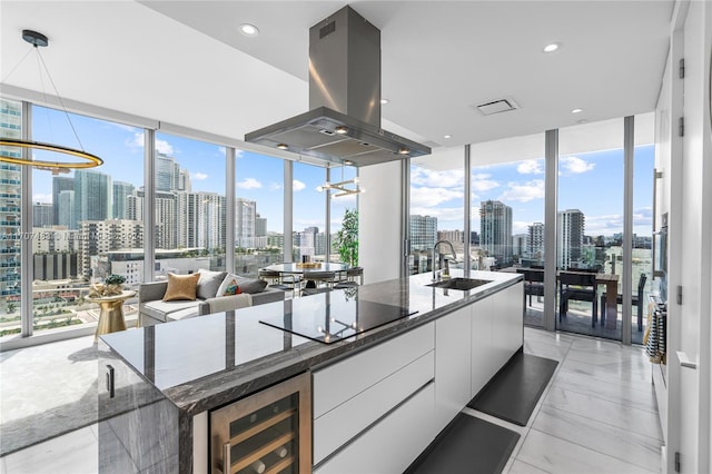 kitchen featuring floor to ceiling windows, white cabinetry, sink, and island range hood