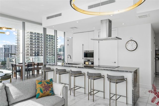 kitchen featuring white cabinetry, sink, double oven, dark stone counters, and island range hood