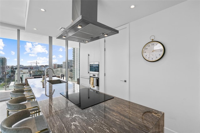 kitchen featuring island exhaust hood, a kitchen bar, expansive windows, black electric cooktop, and sink