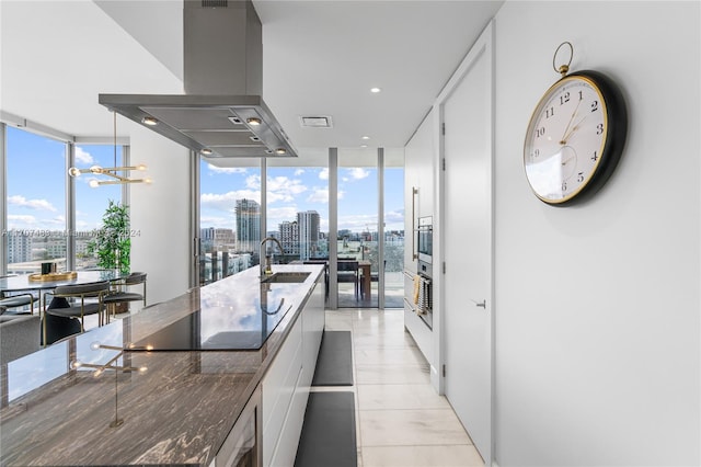 kitchen featuring floor to ceiling windows, sink, an inviting chandelier, island range hood, and white cabinets