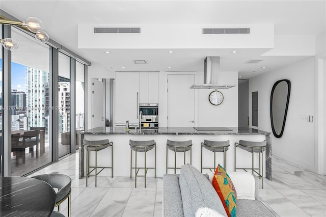 kitchen with a kitchen breakfast bar, range hood, dark stone counters, black electric stovetop, and white cabinets