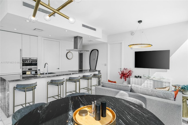 kitchen with white cabinets, a kitchen bar, island range hood, and dark stone countertops