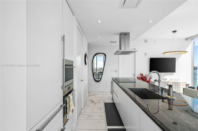 kitchen with island exhaust hood, stainless steel oven, white cabinetry, and sink