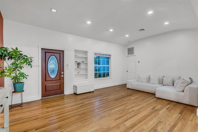 living room featuring built in features, light wood-type flooring, and lofted ceiling