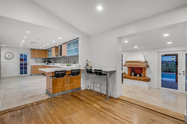 kitchen with light hardwood / wood-style flooring, a fireplace, tasteful backsplash, kitchen peninsula, and a breakfast bar area