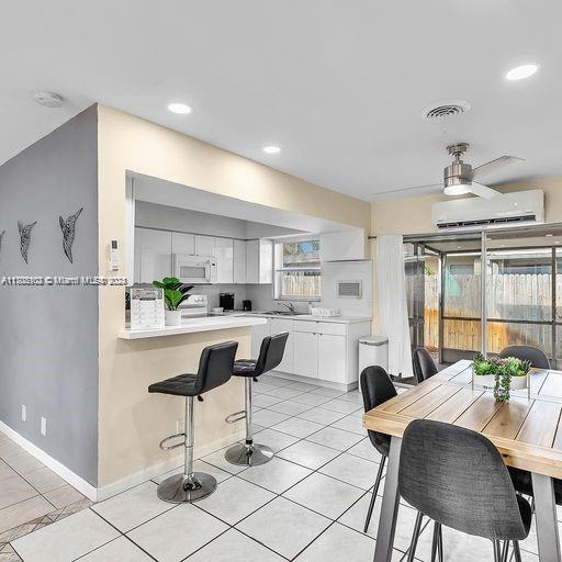 kitchen with a wall mounted AC, ceiling fan, sink, light tile patterned floors, and white cabinetry