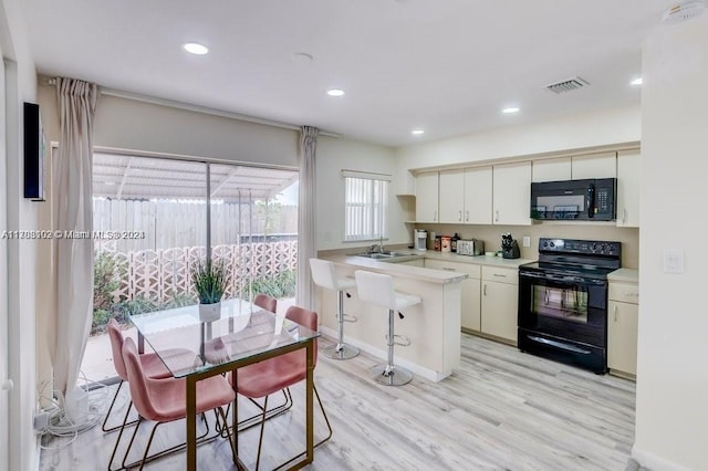 kitchen with kitchen peninsula, light wood-type flooring, black appliances, white cabinets, and a breakfast bar area