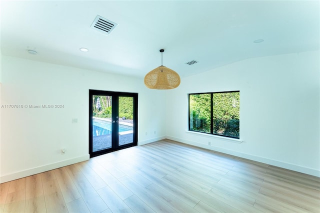 empty room with lofted ceiling, plenty of natural light, french doors, and light hardwood / wood-style flooring