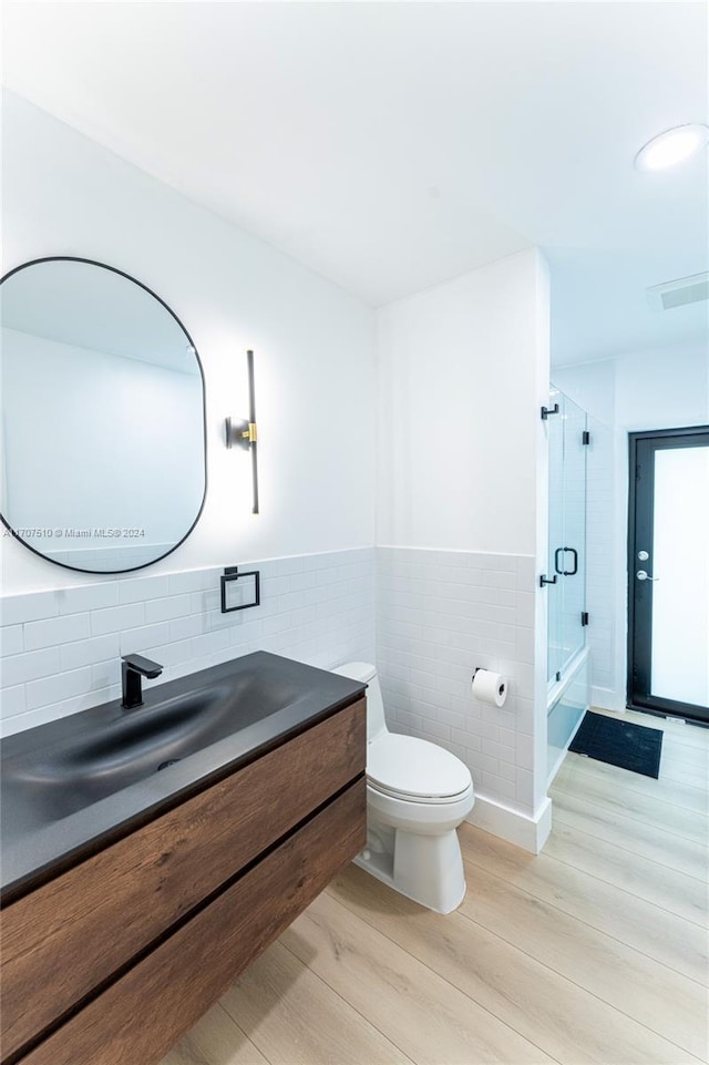 full bathroom with vanity, combined bath / shower with glass door, hardwood / wood-style flooring, toilet, and tile walls