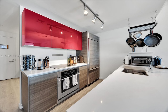 kitchen featuring stainless steel oven, sink, light hardwood / wood-style flooring, track lighting, and black electric stovetop