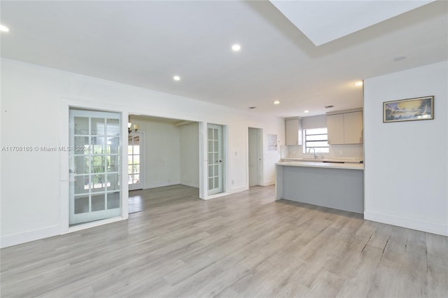 unfurnished living room with light hardwood / wood-style flooring, a notable chandelier, and sink