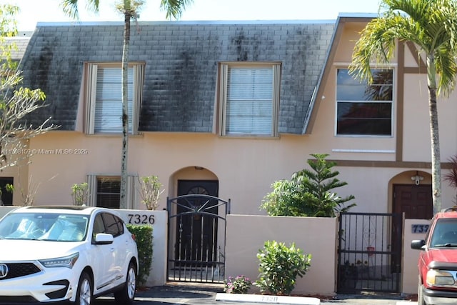 view of front facade with a fenced front yard, a gate, mansard roof, and stucco siding