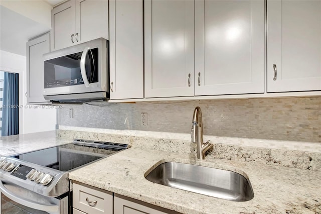 kitchen with decorative backsplash, stainless steel appliances, light stone counters, and sink