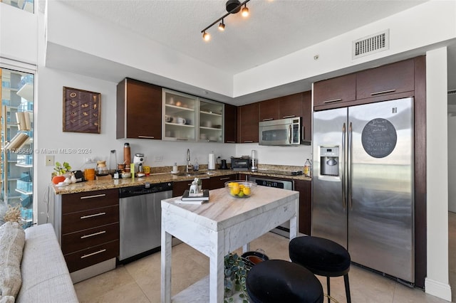 kitchen featuring sink, stainless steel appliances, light stone counters, a textured ceiling, and dark brown cabinets